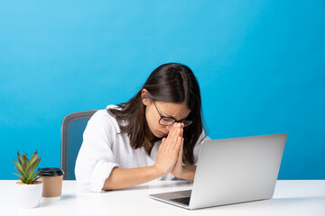 Wall Mural - Hispanic pretty young woman praying at laptop isolated on blue background.