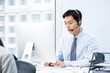 © Atstock Productions - Asian male office worker wearing headset with microphone browsing computer and speaking to customer during work
