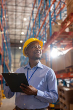 Smiling African American Young Male Worker Holding Clipboard Looking Up While Standing In Warehouse