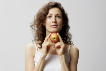 Wall Mural - Smiling lovely cute curly beautiful woman in basic white t-shirt pulls apple enjoy healthy food posing isolated on over white background. Natural Eco-friendly products concept. Copy space