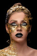 Closeup portrait of beautiful young woman with golden foil on face. Creative golden makeup on black background