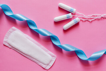 Wall Mural - top view of tampons and soft panty liner near blue satin ribbon on pink background.