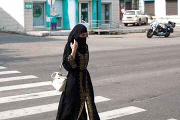 A Muslim woman in a black outfit and a burqa walking along a pedestrian crossing on a city street.