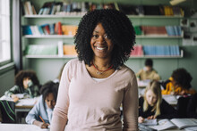 Portrait Of Confident Teacher With Curly Hair Standing In Classroom