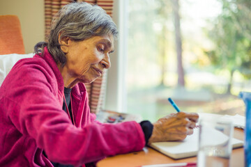 Old Asian Indian woman writing in journal or notebook, UK