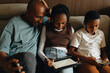 © Maskot - Father sitting with daughter and son using wireless technologies at home