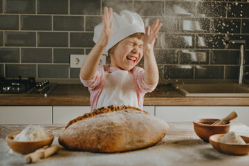 Little girl in apron making bread sprinkling flour on wooden table