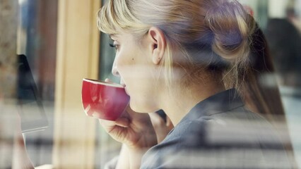 Aufkleber - A happy businesswoman enjoying a cup of coffee in a cafe while using her wireless tablet. Young woman sitting in a cafe browsing on her digital tablet and drinking a cup of tea.