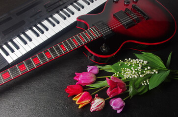 Canvas Print - Electric guitar, synthesizer keyboard, bouquet of tulips and lilies of the valley on a black table.