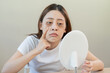 © KMPZZZ - Bored, insomnia asian young woman, girl looking at mirror, without makeup, touch under eyes with problem of dark circles, puffiness, swollen or wrinkles on face. Sleepless, sleepy people, copy space