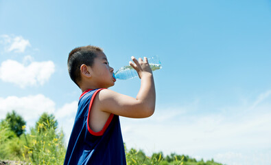 Little asian boy drinking water against blue sky