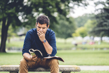 Caucasian male sitting in the park and reading the Holy Bible