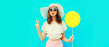 Portrait Of Beautiful Young Woman Blowing Her Lips Sending Air Kiss With Yellow Balloon Wearing Summer White Straw Hat On Blue Background