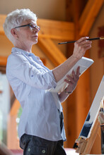 Middle-aged Woman Painting On Canvas In Her Cottage