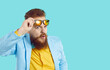 Funny chubby bearded man looks at you with expression of suspicion, doubt and disbelief on his face. Skeptical and suspicious man looking out from under glasses on light blue background. Web banner.