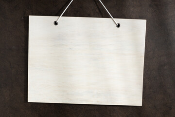 Blank white wooden sign hanging on dark textured wall. Mock up template