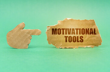 On a green surface, a cardboard hand points to a sign with the inscription - Motivational Tools