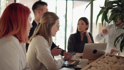 Smiling young successful people, colleagues talking, discussing business ideas with a laptop and drinking coffee, enjoying pleasant business conversation in cafe during meeting