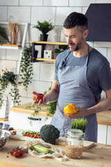 Wall Mural - Handsome father, strong young man cooking healthy vegetable salad with fresh organic ingredients, tasty food in the kitchen at home . Men doing chores. Ripe pepper, tomato, cucumber