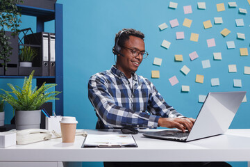 Wall Mural - helpline support agent wearing headset and using work computer while being on telephone call with cl