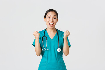 Wall Mural - Covid-19, healthcare workers and preventing virus concept. Hopeful and relieved, joyful asian pretty female doctor, physician rejoicing with fists pump, congrats or praise someone, winning