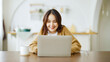 © Monster Ztudio - Smiling asian young woman working on laptop at home office. Young asian student using computer remote studying, virtual training, e-learning, watching online education webinar at house