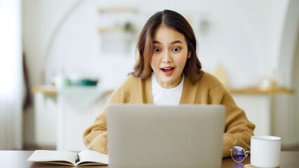 Smiling asian young woman working on laptop at home office. Young asian student using computer remote studying, virtual training, e-learning, watching online education webinar at house