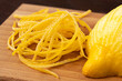 Heap of peeled lemon zest on wood chopping board next to half of peeled lemon.