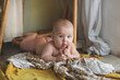 cute european baby 5 months old lies on a blanket on the floor. A child wearing amber teething beads in a real interior