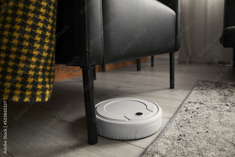 Modern robot vacuum cleaner under black armchair in room