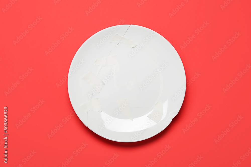 Broken ceramic plate with adhesive tape on red background