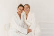 © Look! - Beautiful young ladies with fair skin use patches to treat puffiness under eyes on white background. Blondes wear white bathrobes after spa. Skin care and hydration concept