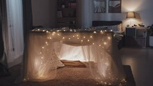Tilting Down View Of Dreamlike Blanket Fort With Lit Garland In Bedroom At Night