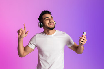 Poster - Handsome young Arab man listening to music in headphones, using new smartphone app and dancing in neon light