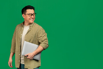 Online offer. Mature asian man holding laptop and looking back at free space over green studio background