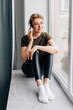 © F8  \ Suport Ukraine - Young woman talking on the smartphone while sitting on the windowsill at home, chatting with friends. Attractive female in casual wear sits and holding phone conversation