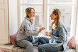 © Look! - Two young caucasian female friends on coffee break spend time together sitting on windowsill day. Blondes wear jeans and shirts. People, communication and friendship concept