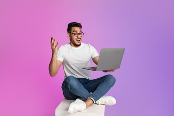 Poster - Excited young Arab man sitting cross legged with laptop, feeling overjoyed over huge online sale in neon light