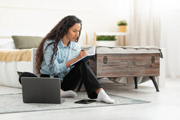 Poster - Woman sitting on floor, using computer and writing in notebook
