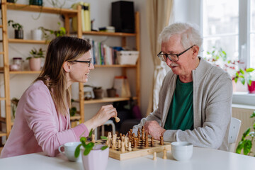 Adult daughter visiting her senior father at home and playing chess together.