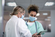 © ReeldealHD images - Two female medical practitioners discussing patient treatment using a digital tablet wearing face masks