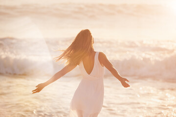 Canvas Print - a young woman enjoying her time at the beach. Carefree woman enjoying the sun on the beach. Back of a carefree content woman celebrating and enjoying the sunset on the beach