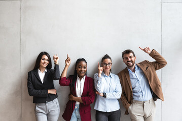 Group of young happy successful business team people pointing finger up and smiling. Freelancers or exchange students showing above and smile looking at the camera. 