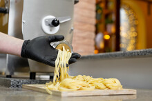 Pasta, Noodles Come Out Of A Professional Machine, Cook Opens It And Twists It On A Wooden Board