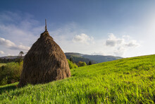 Haystack On A Grassy Rural Field In Mountains. Beautiful Countryside Landscape With Forested Hills On A Fine Summer Day