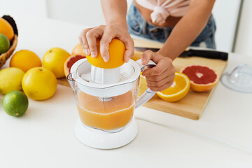 Wall Mural - Female hands and citrus juicer during fresh orange juice preparation