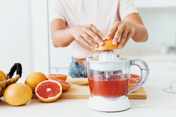 Wall Mural - Female hands and citrus juicer during fresh grapefruit juice preparation