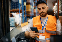 Forklift Operator Text Messaging On Cell Phone While Working At Distribution Warehouse.