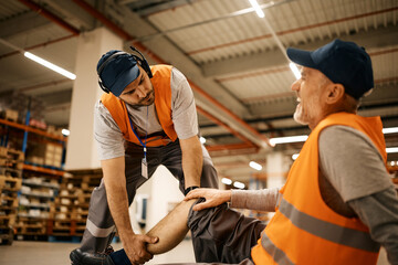 Poster - Warehouse worker helps his mature coworker who injured leg while working in storage compartment.