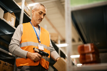 Wall Mural - Mature warehouse worker scanning packages with bar code reader at storage compartment.